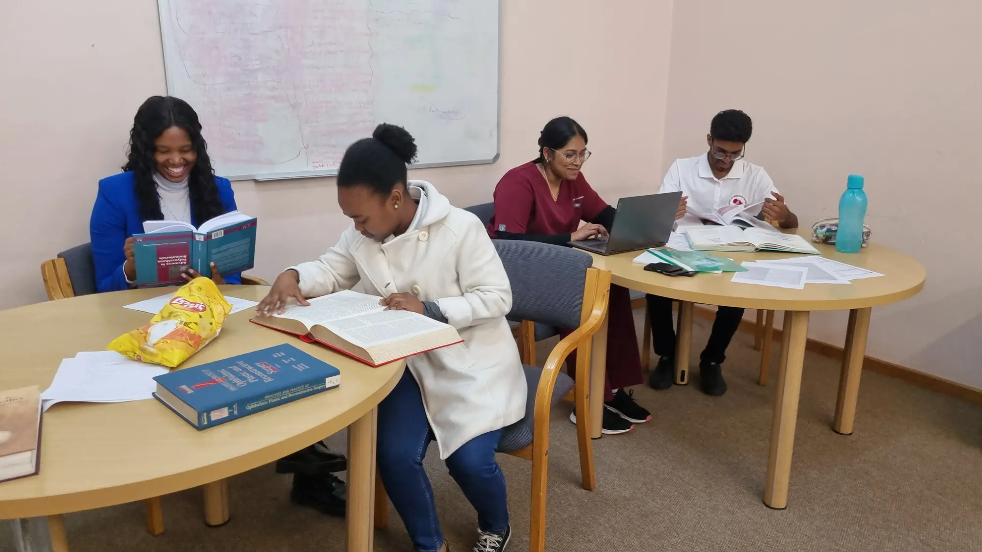 Medical and science students studying together around a table with textbooks, papers and a laptop